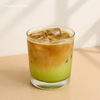 Iced matcha espresso latte in a clear glass with layered green matcha, creamy milk, and espresso on top, styled with a wooden tray and minimal aesthetic.