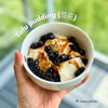 Homemade tofu pudding (豆花) topped with brown sugar syrup and chewy tapioca pearls, served in a white bowl and held in hand by a window.