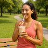 A smiling woman in a pink tank top drinks bubble tea while standing in a sunny park, promoting a balanced and healthy lifestyle.